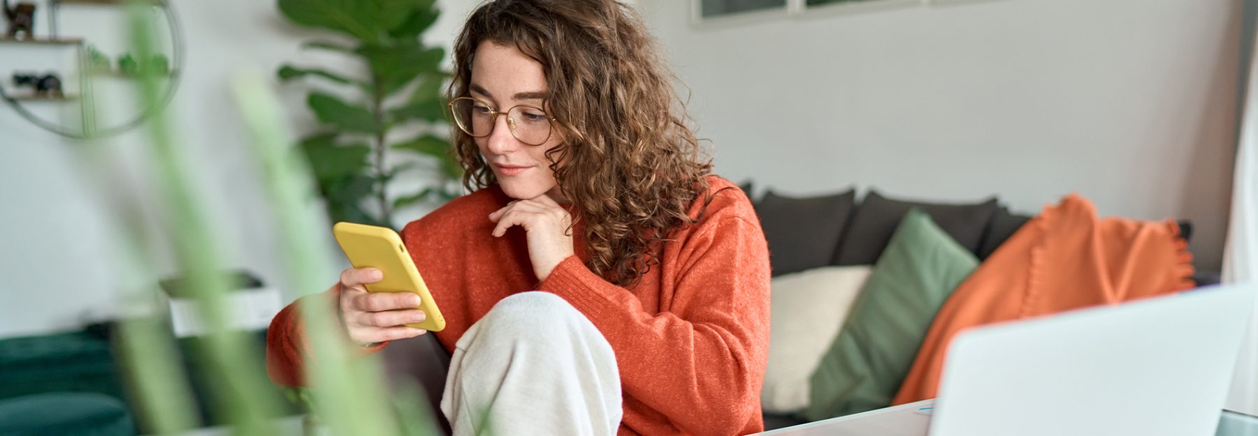 woman wearing glasses browsing phone in front of laptop